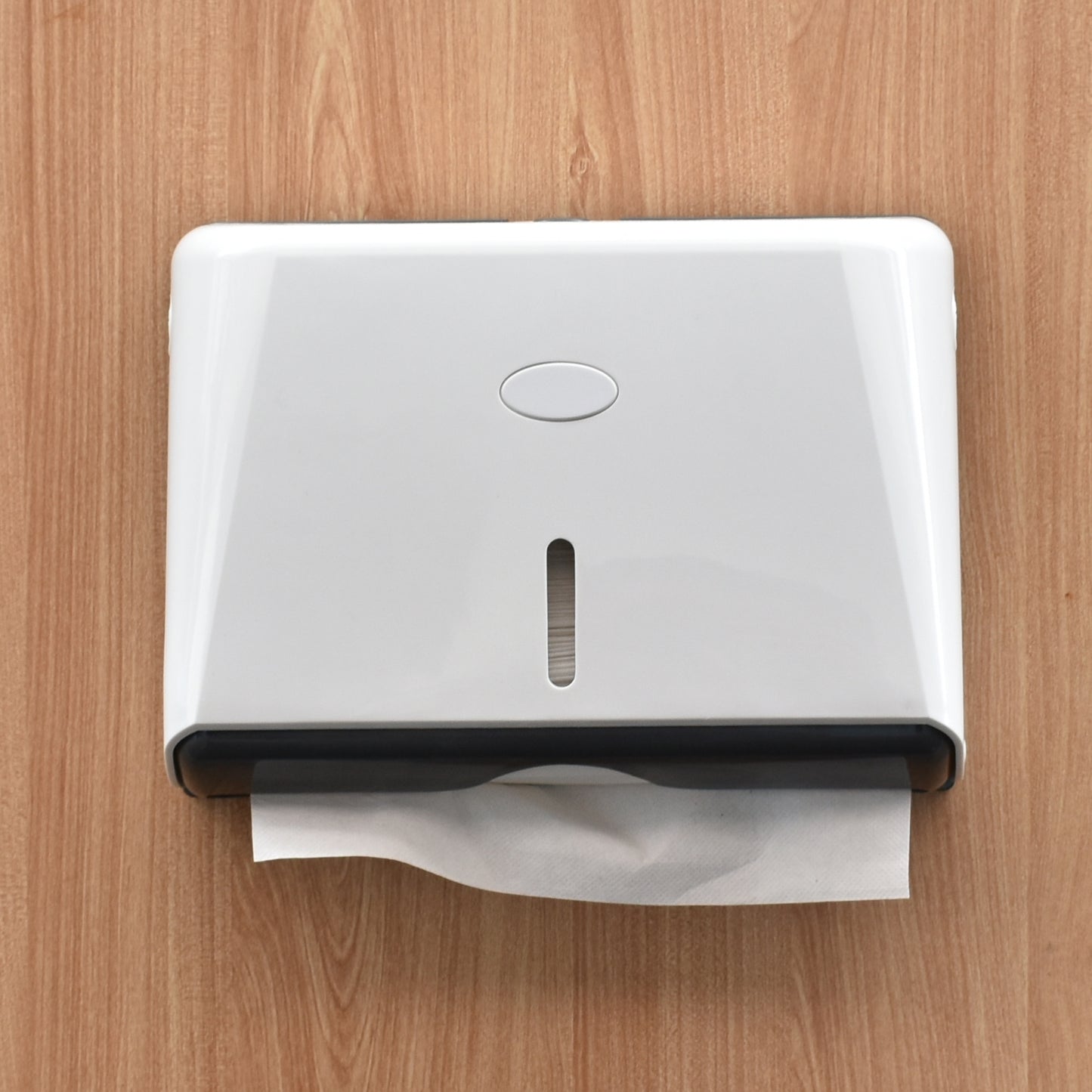 A white wall-mounted tissue dispenser with a tissue paper partially pulled out, set against a light brown wood-grain wall.